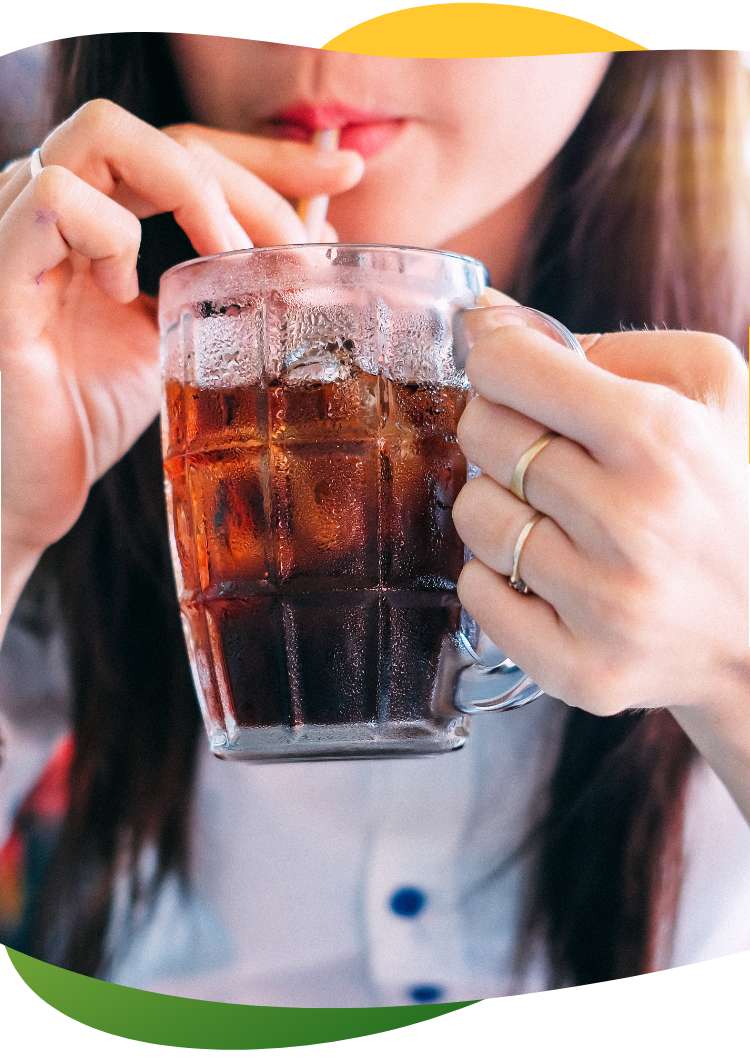 A young woman with long, brown hair holds a tall glass with her hand and drinks a carbonated drink with a straw out of it