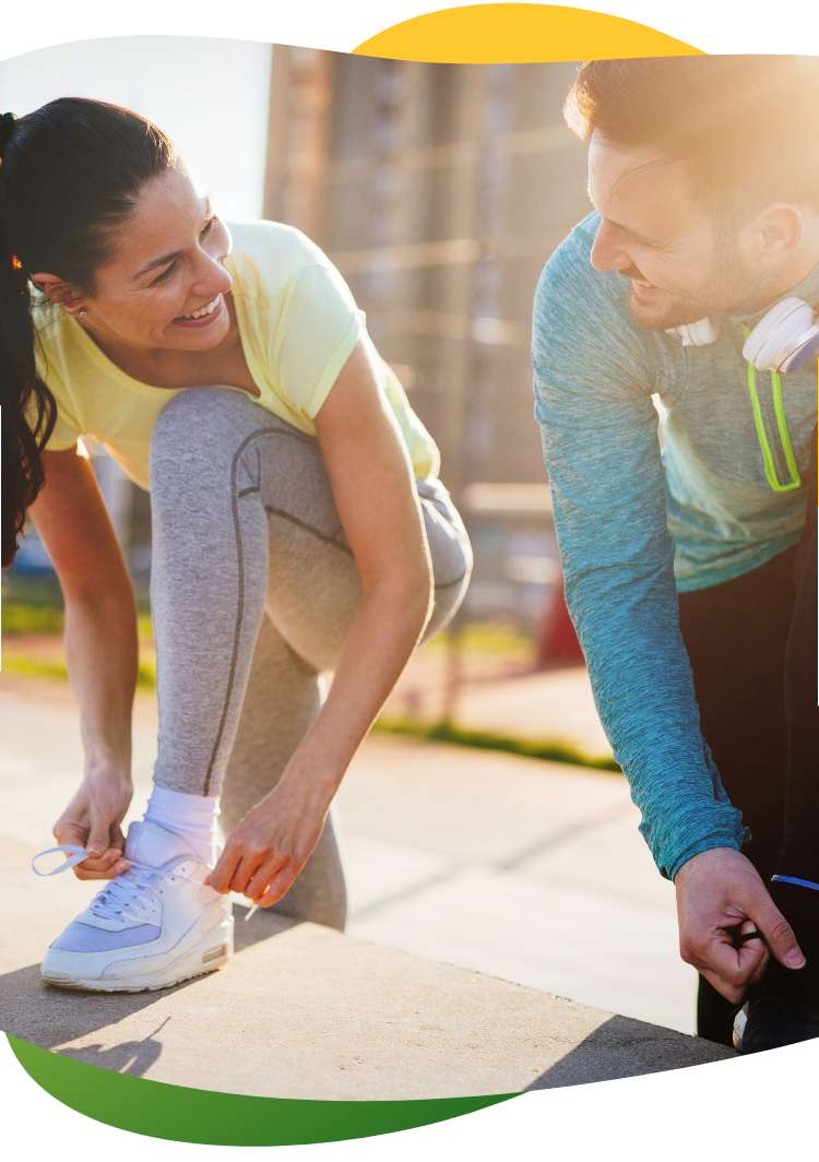 A woman and a man looking at each other while kneeling on the side of the road and tying their jogging shoes