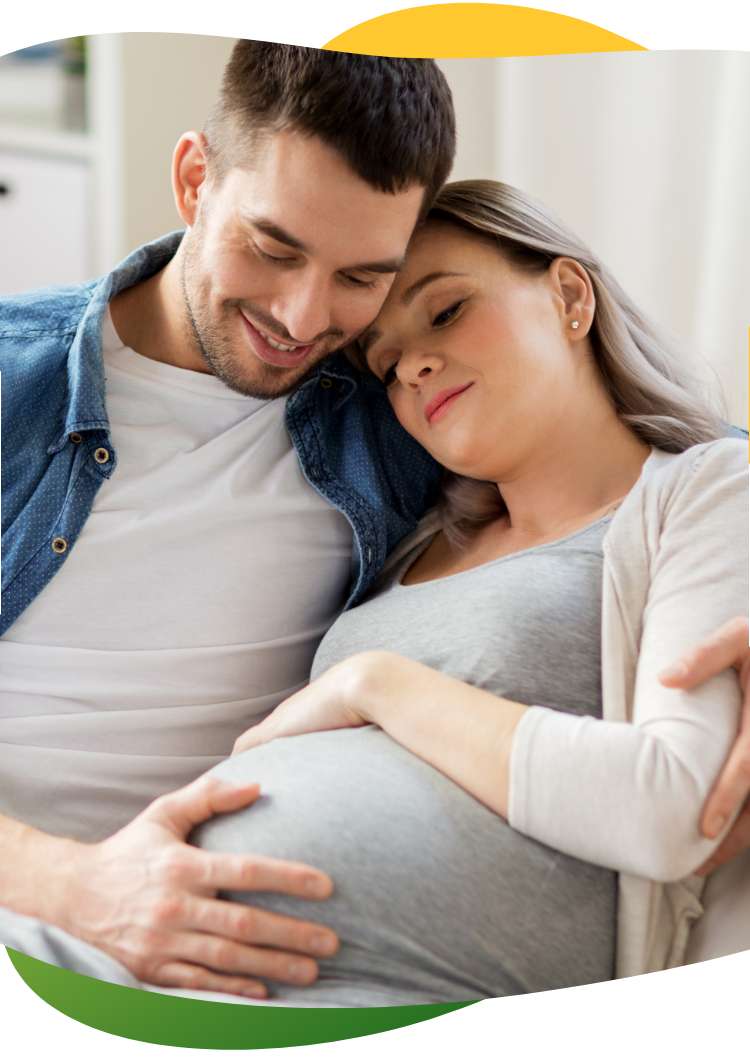 A pregnant woman suffering from bloating, sitting on the sofa with her eyes closed. Her partner comforts her and holds her in his arms