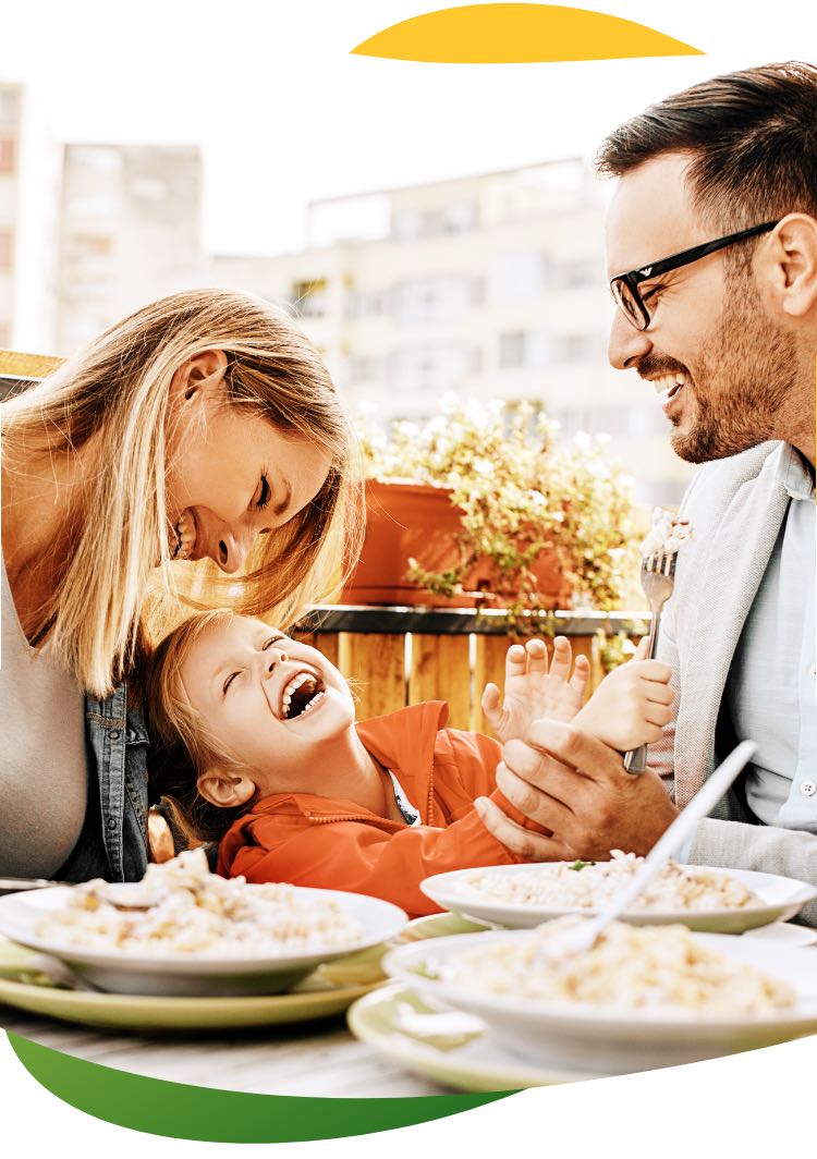 Young parents having a meal at the dining table, wearing their work clothes with their child sitting between them. They are laughing and having a good time together